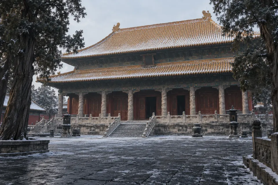The Temple of Confucius at Qufu, red walls and yellow-tiled halls of the Dacheng Hall among ancient cypresses, a light dusting of snow, quiet pale morning