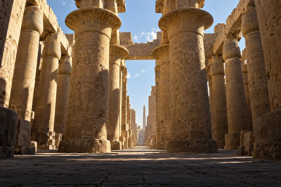 The Great Hypostyle Hall at Karnak, towering papyrus-bud columns and an obelisk against a pale sky, Amun-Ra's temple precinct at Thebes, hard clear noon sun