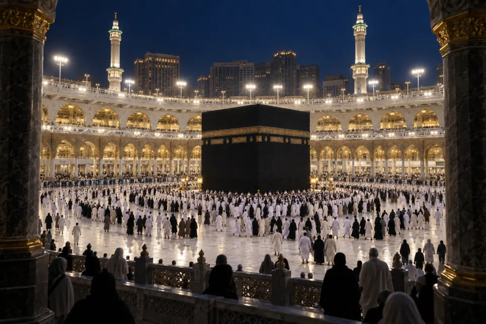 The Kaʿba draped in black at the centre of the Sacred Mosque, Mecca, pilgrims circling in white seen small and from behind, floodlit white arcades, deep blue night